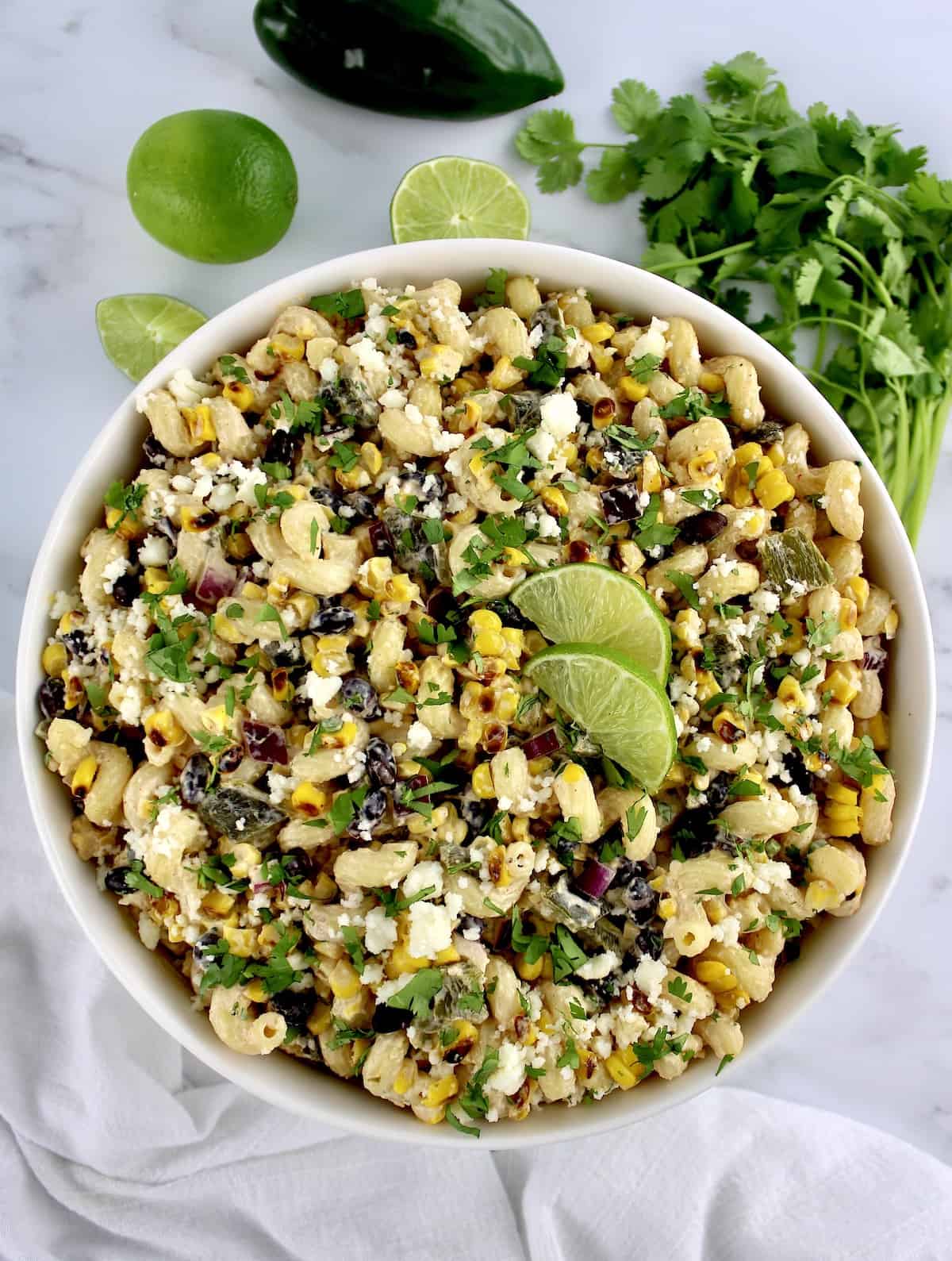 Mexican Street Corn Pasta Salad in white bowl with lime slices and chopped cilantro